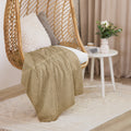 Luxury Sherpa Throw Blanket draped over a wicker hanging chair with textured pillows, next to a white round side table holding a vase with flowers in a cozy, elegant living space.