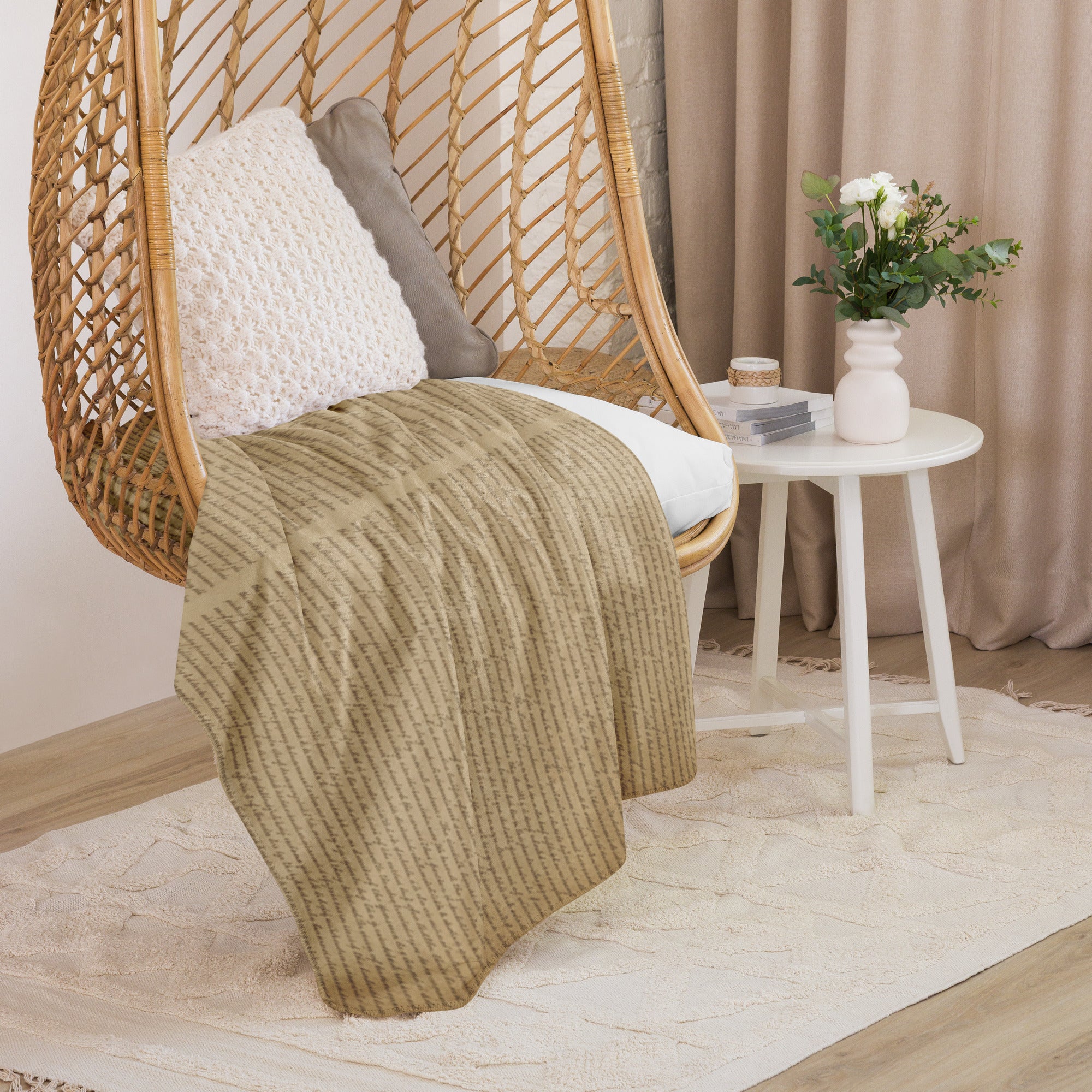 Tan Luxury Sherpa Throw Blanket — Signature Edition draped over a wicker chair with decorative pillows, next to a white side table with a vase of flowers in a cozy, elegant living room setting.